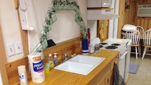 Pieni keittiö, jossa on puinen työtaso, valkoinen pesuallas, liesi ja mikroaaltouuni. Työtasolla on siivoustarvikkeita.