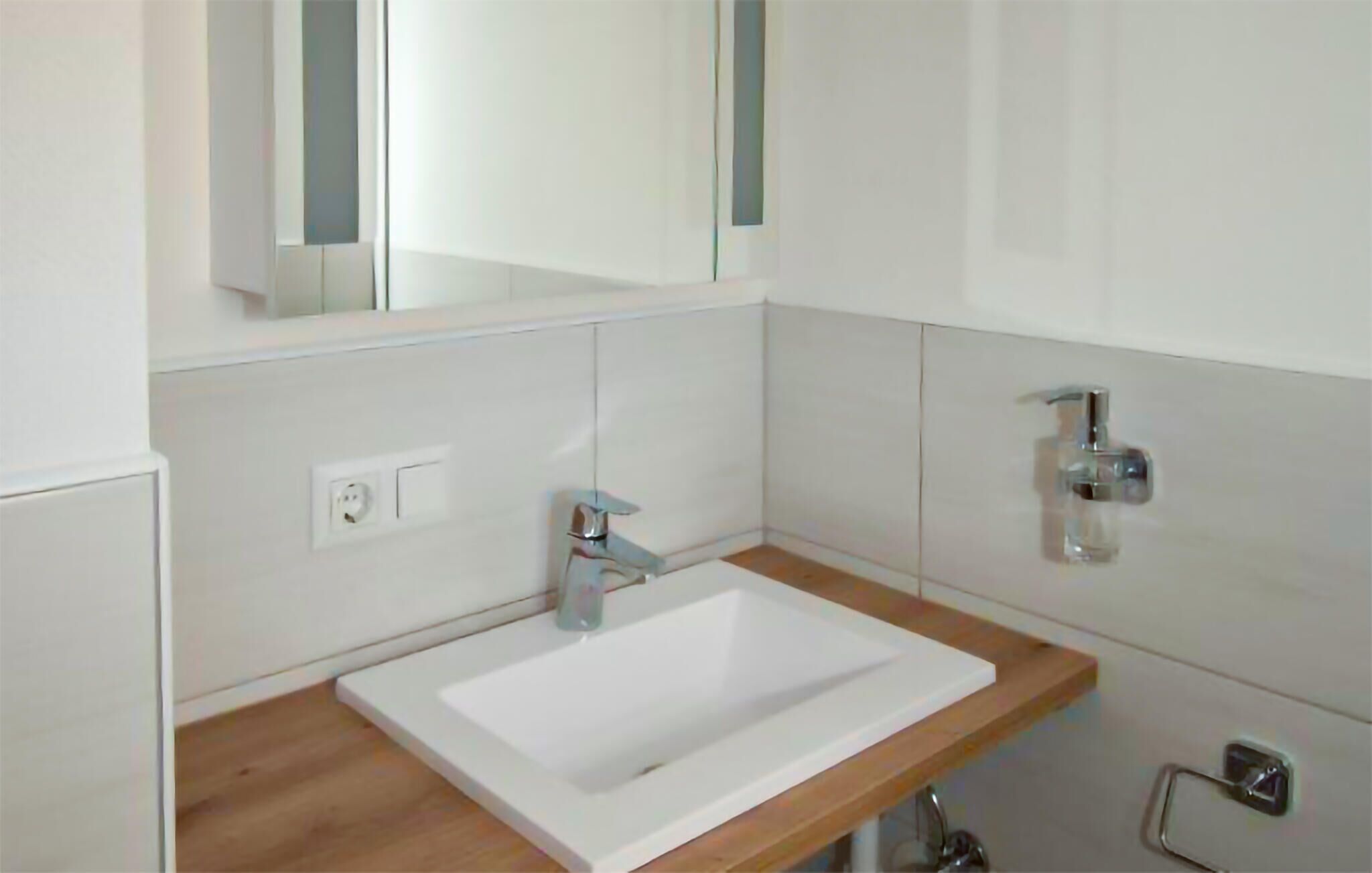 A modern bathroom with a white sink, wooden countertop, and a mirror above.