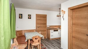A compact room with a wooden bench, a small table, and a kitchen area with white cabinets and a wooden door. - 2 bedroom amazing apartment in Liesing (Liesing)