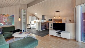 A modern living room with a green sofa, a white coffee table, and a flat-screen TV on a white stand. There is a kitchen area with white cabinets and a black stove. - Amazing home in Tarm with kitchen (Tarm)