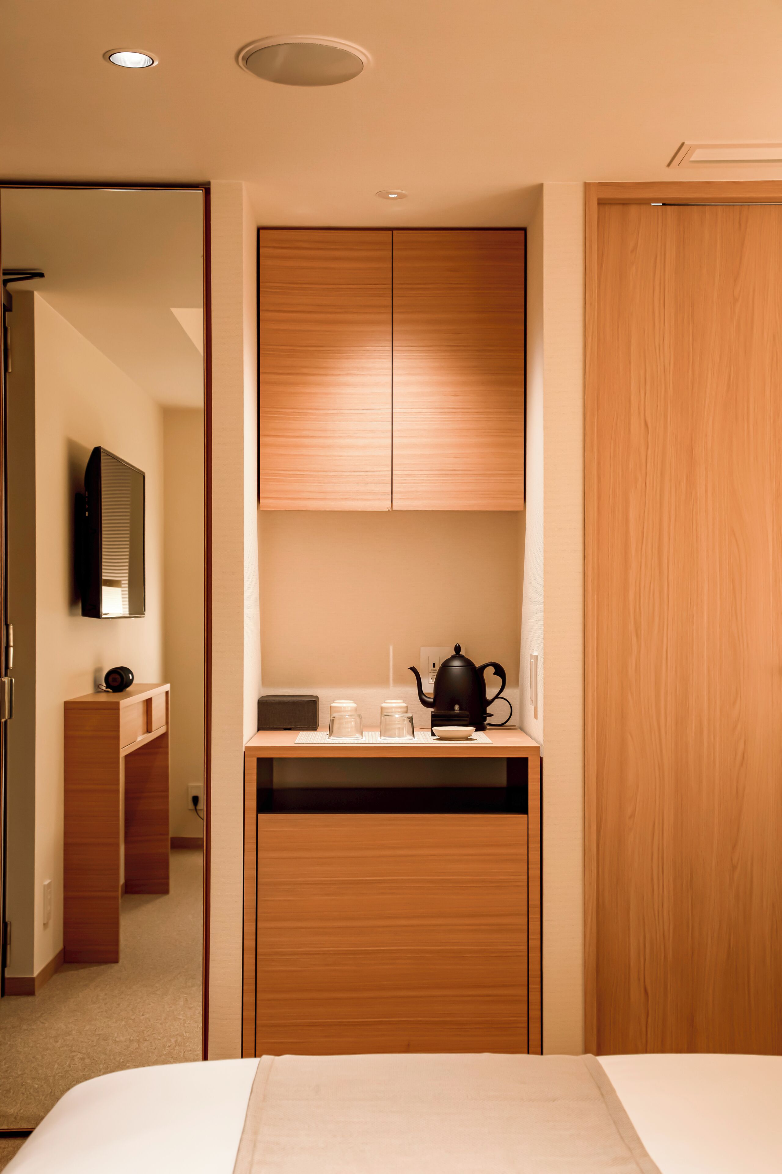 A hotel room with a bed, a wooden wardrobe, a small table with a kettle and cups, and a mirror on the wall.