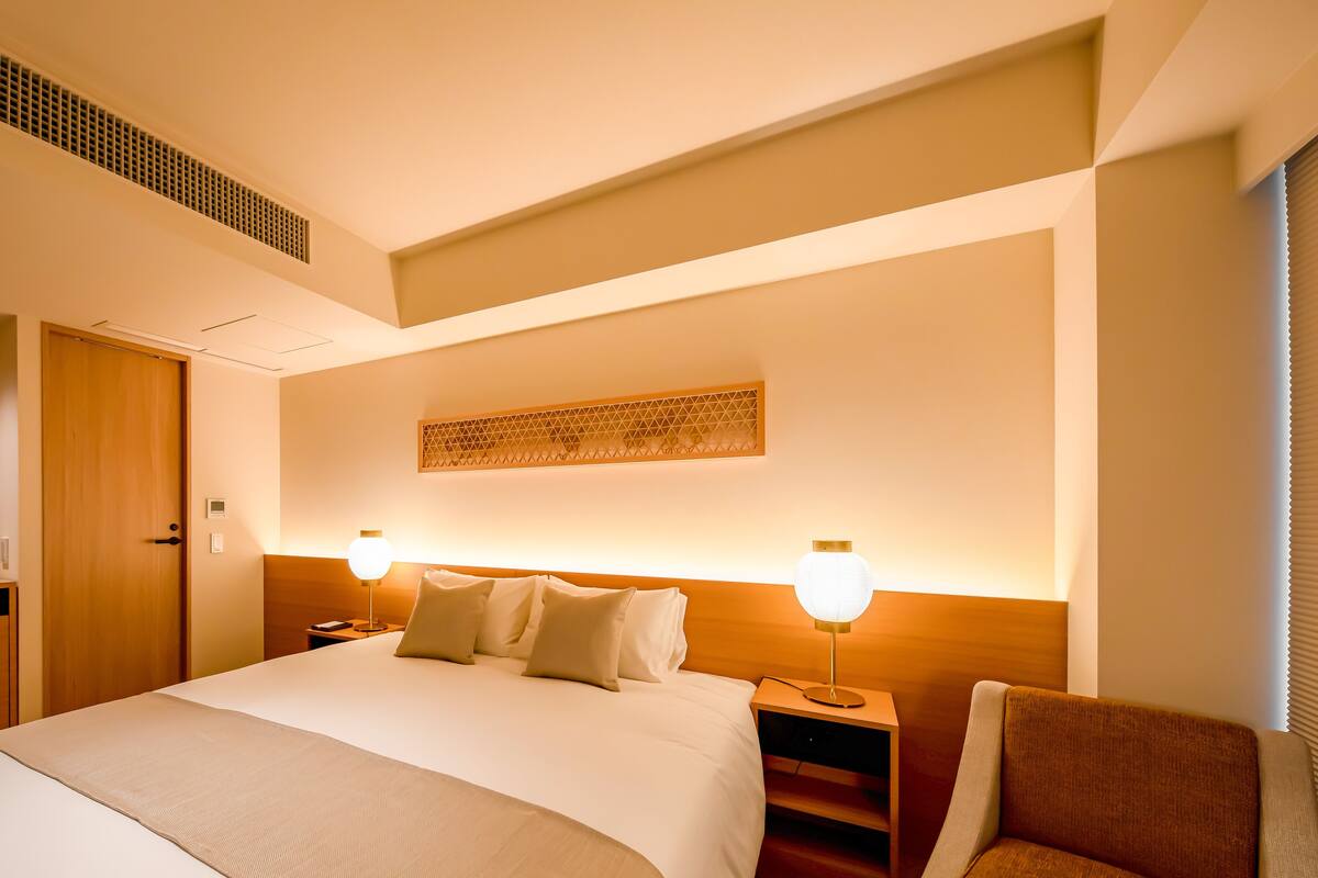 A modern hotel room with a large bed, bedside tables, a wooden wardrobe, and a decorative wall piece.