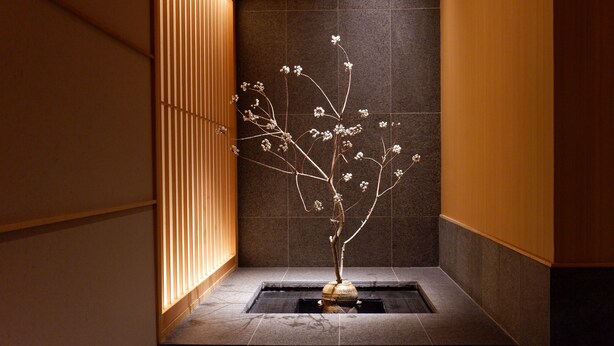 Um jardim interior minimalista com um elemento aquático, painéis de madeira e pisos de pedra escura.