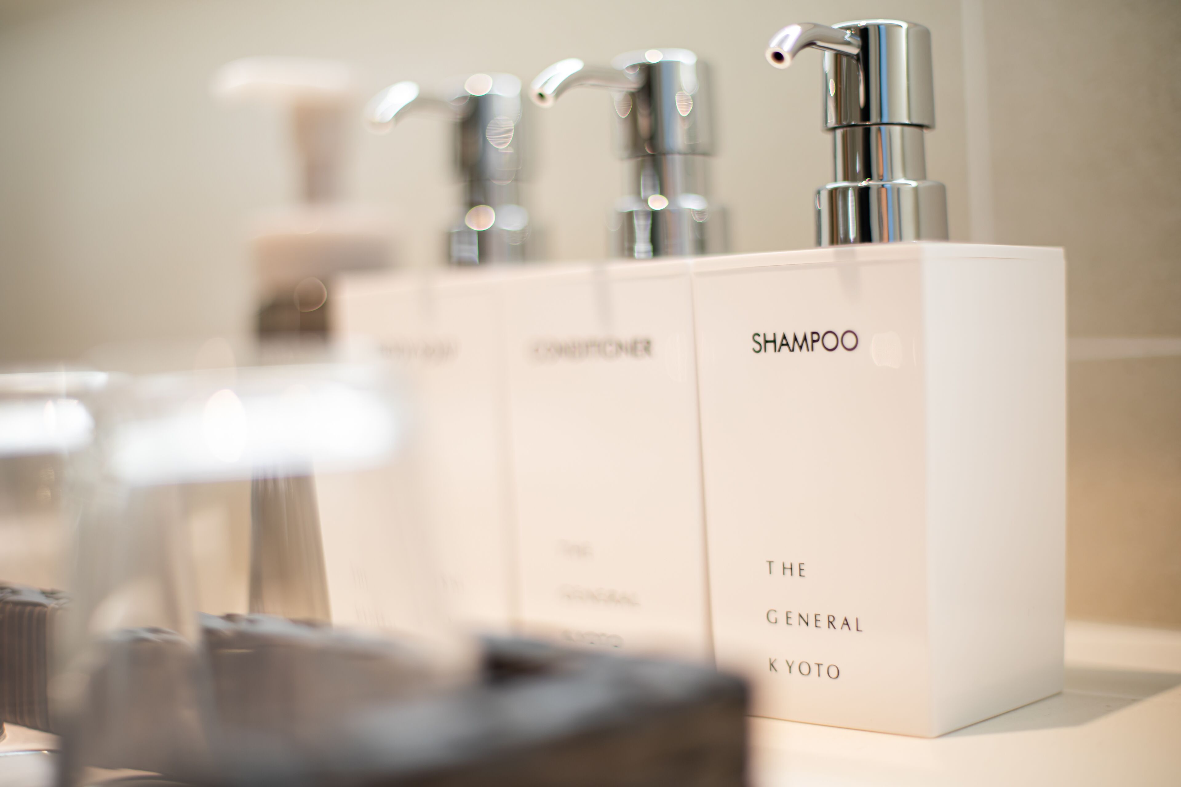 A bathroom with a row of shampoo bottles labeled "The General Kyoto" and a modern faucet.
