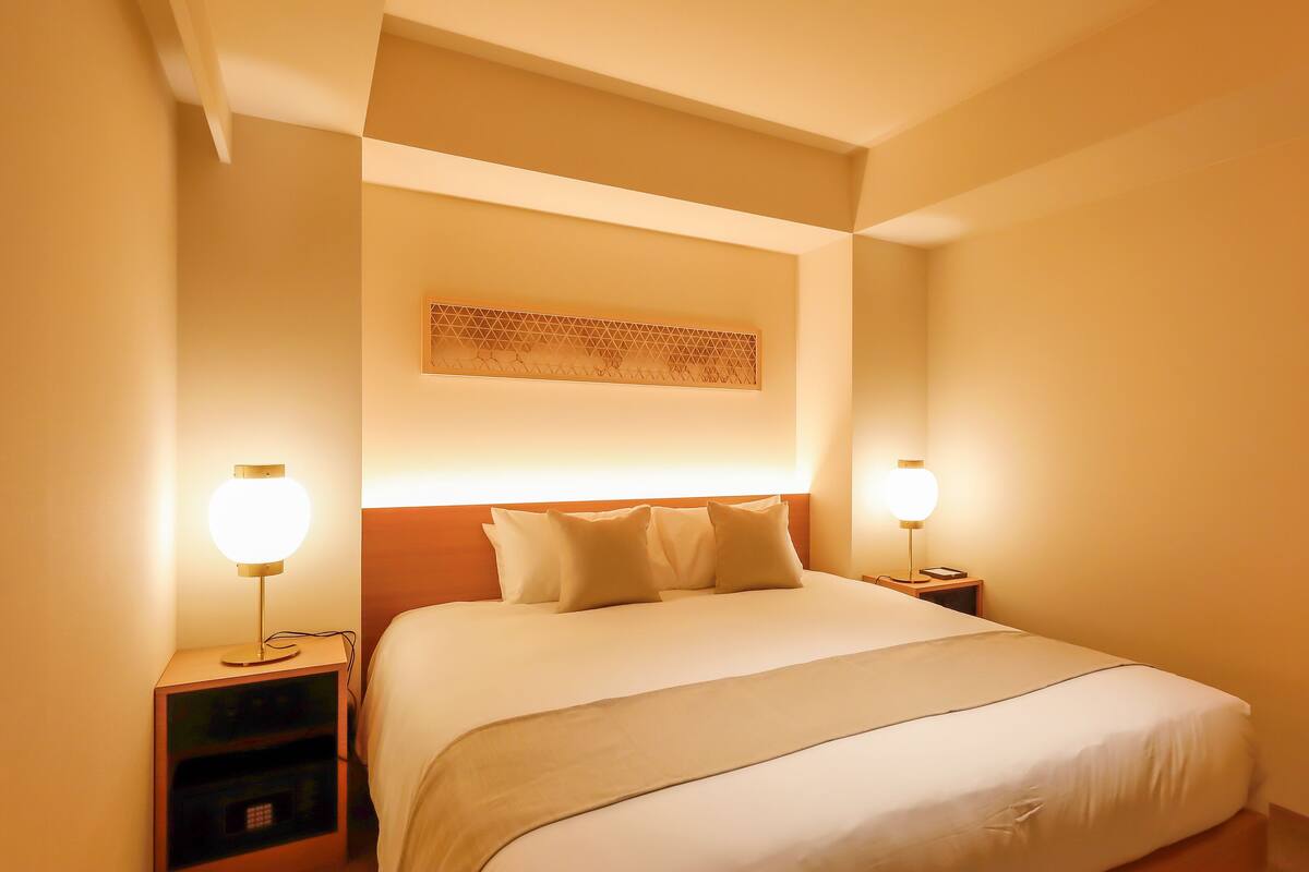 A hotel room with a large bed, two bedside lamps, a nightstand, and a wall-mounted TV.