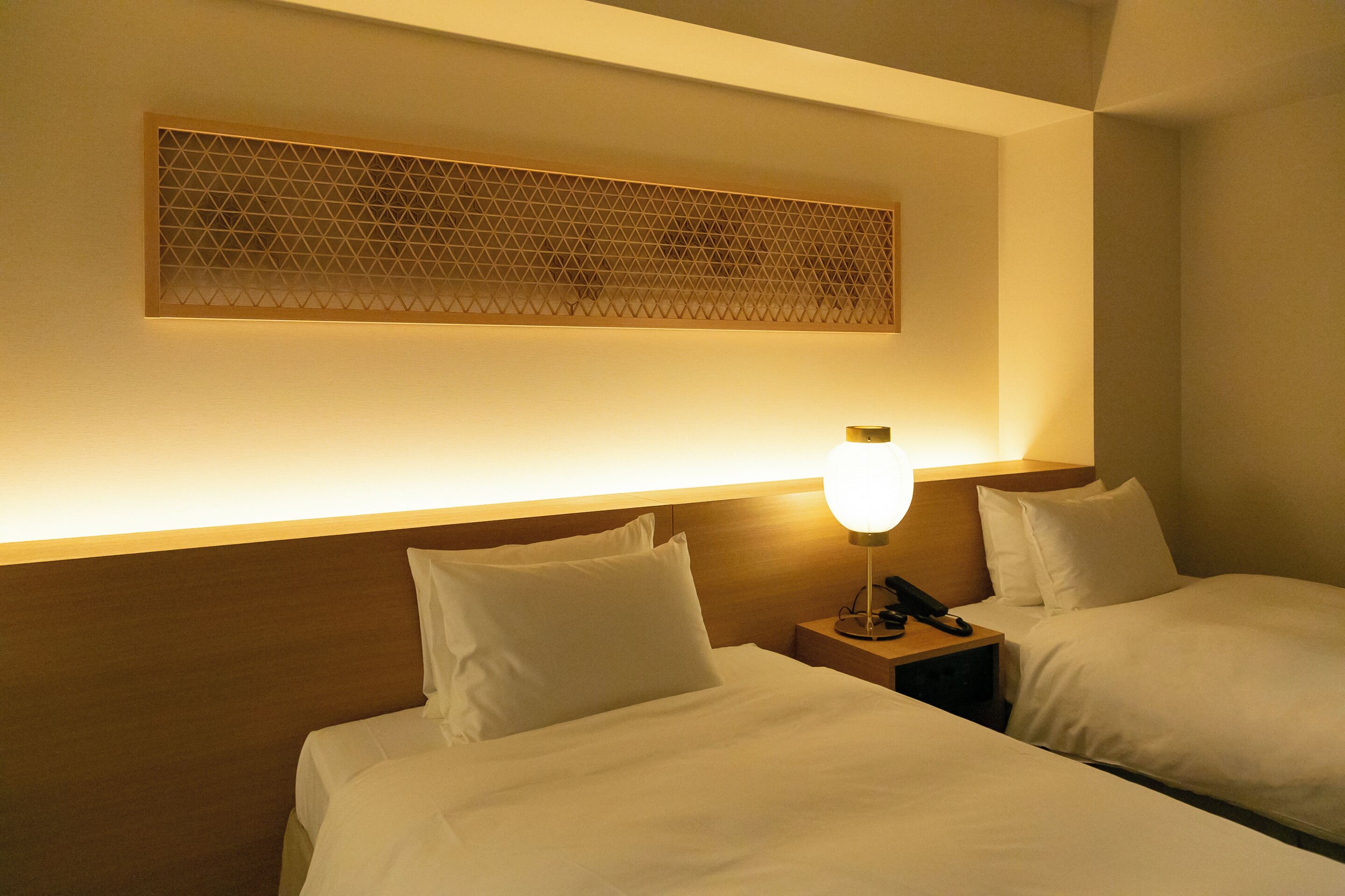 A hotel room with two beds, a nightstand with a lamp, and a decorative wall panel.