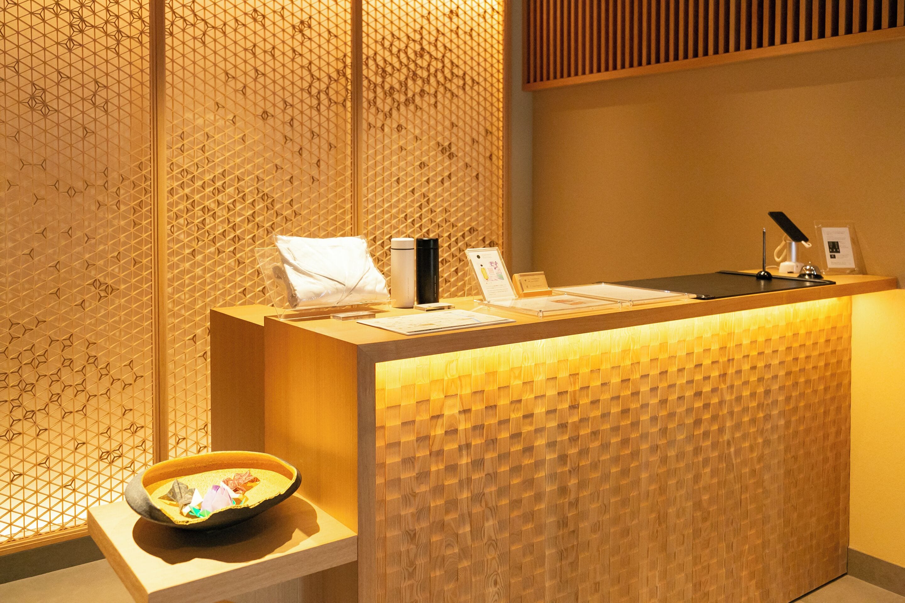 A reception desk with a wooden panel design, a white pillow, a black speaker, and a bowl on a small table.