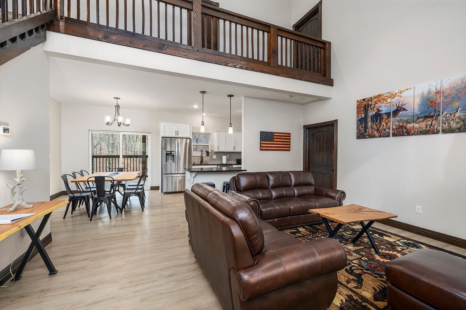 A spacious living area with a high ceiling, a dining table with chairs, a kitchen area, and a large window.