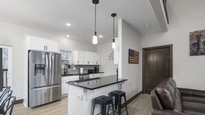 Una cocina moderna con electrodomésticos de acero inoxidable, una isla central con taburetes de bar y una puerta de madera.