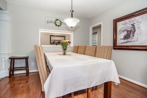 A dining room with a long table, striped chairs, a vase with flowers, and a framed picture on the wall.