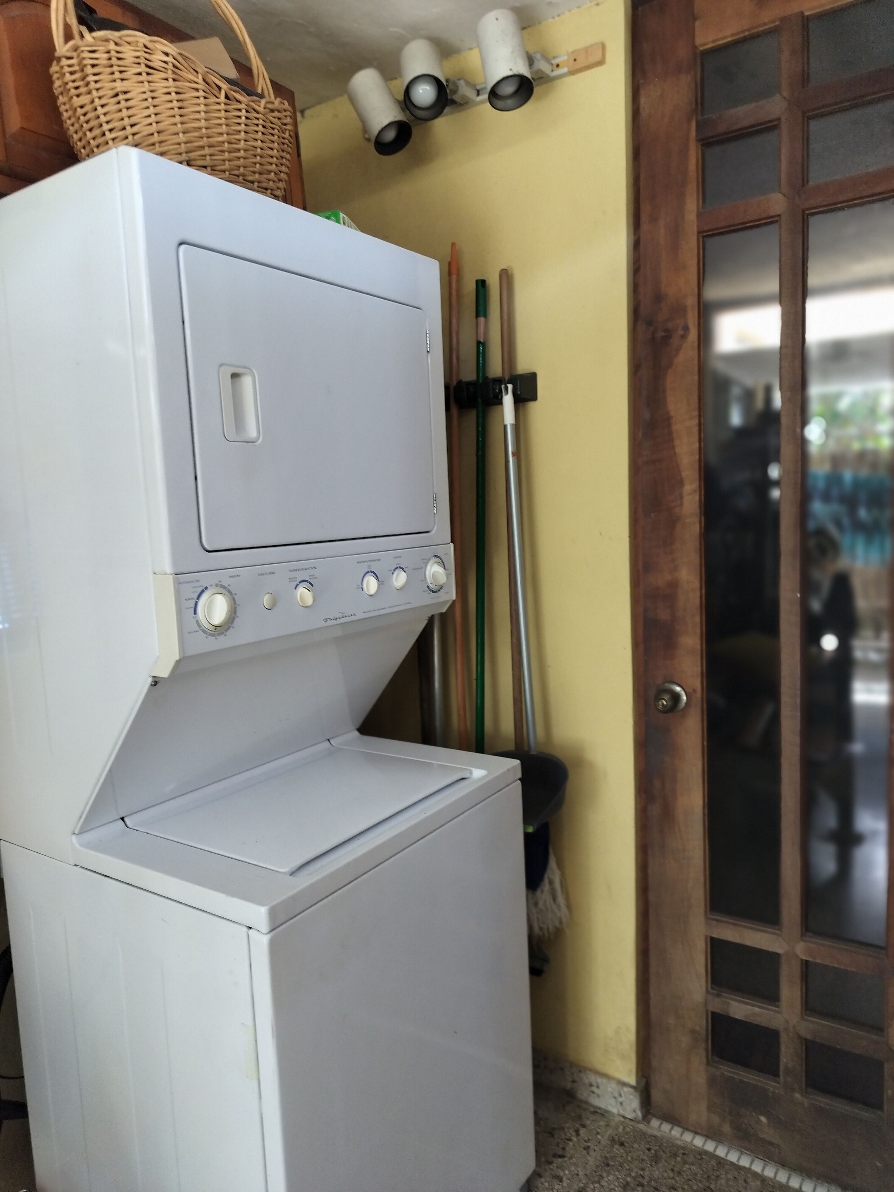 A stacked washer and dryer unit with a basket on top, a mop, and a door with a window.