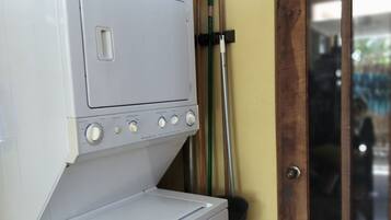 A stacked washer and dryer unit with a basket on top, a mop, and a door with a window.