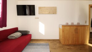 A room with a red sofa, a wooden cabinet, a TV, and a window. - Ferienwohnung mit Ausblick (Dalaas Wald)