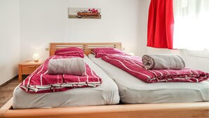 A double bed with two pillows and a blanket, a nightstand with a lamp, and a painting on the wall. - Ferienwohnung mit Ausblick (Dalaas Wald)