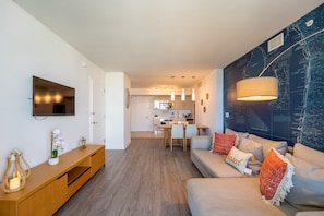 A modern living room with a sofa, a TV, and a dining area in the background.