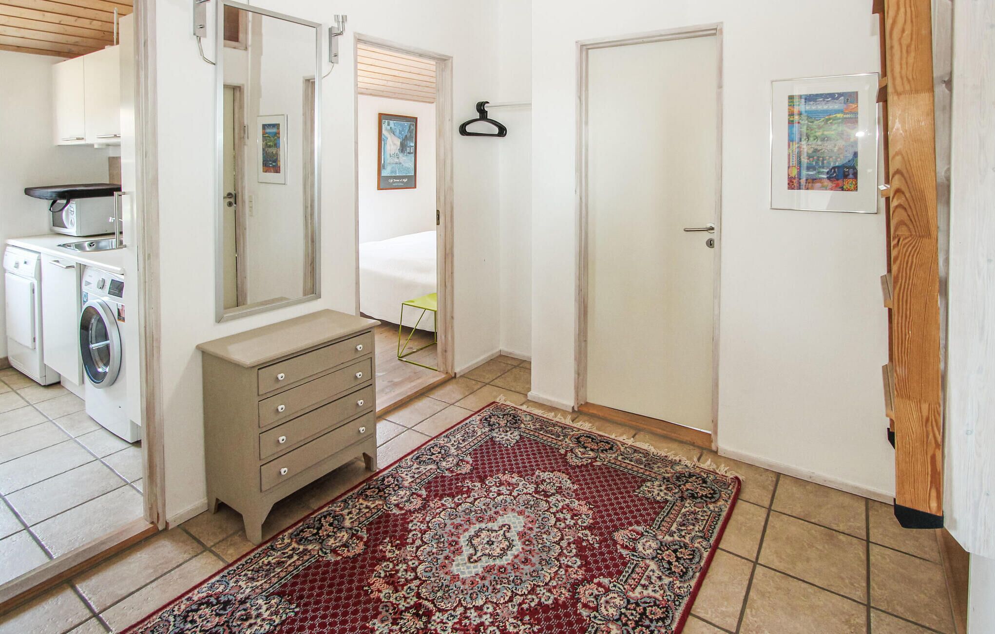 Une pièce équipée d’un lave-linge, d’une commode, d’un miroir, d’une porte et d’un tapis à motifs.