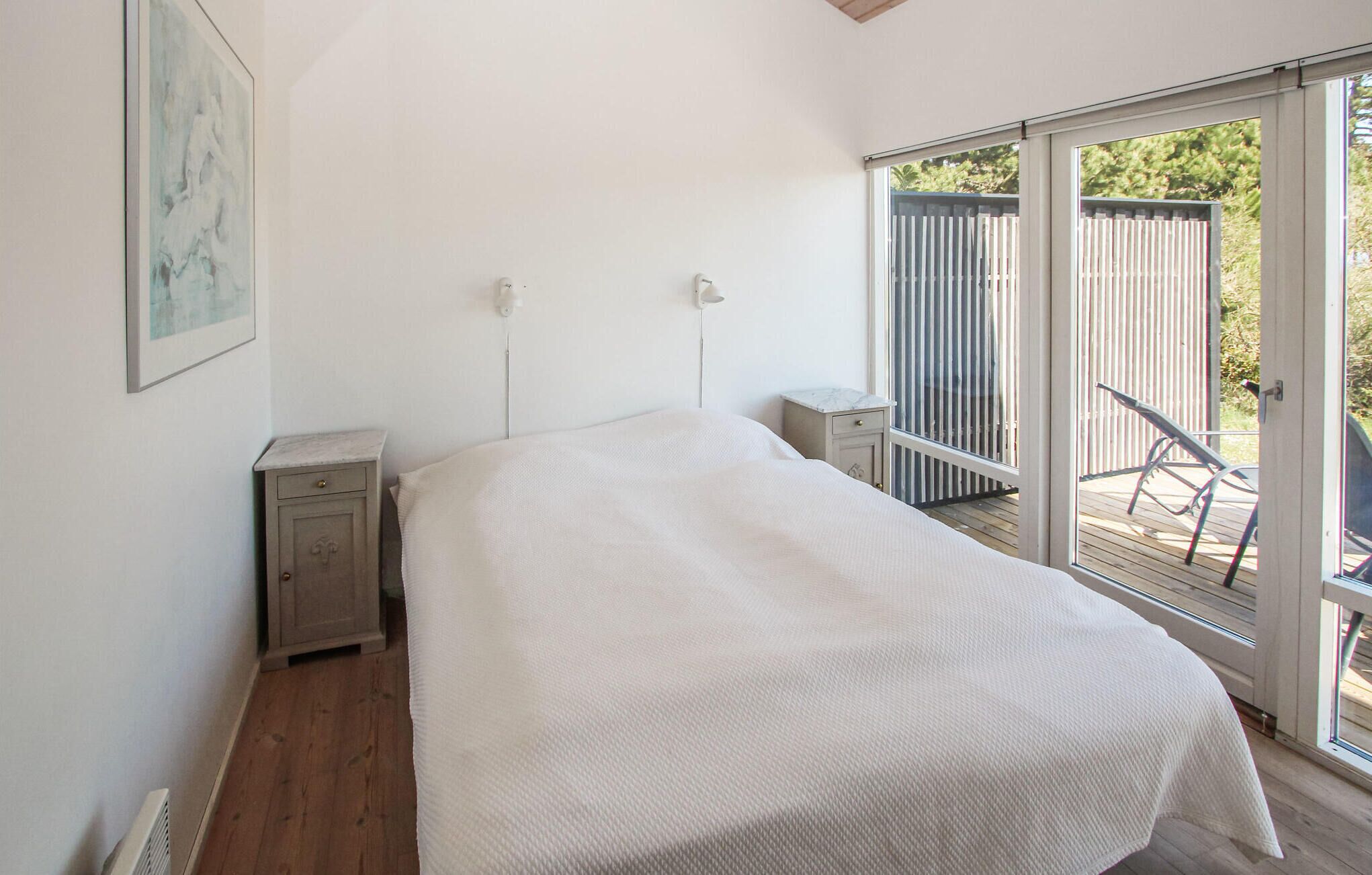 Camera da letto con un letto, comodini, un tavolino e una porta scorrevole in vetro che dà su uno spazio esterno con una sedia.