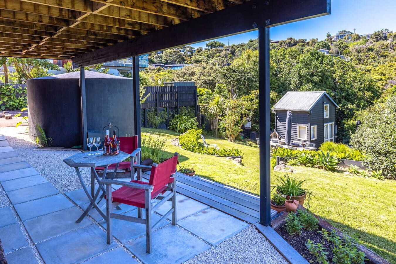 A covered outdoor seating area with a table and chairs, a large cylindrical structure, and a house in the background.