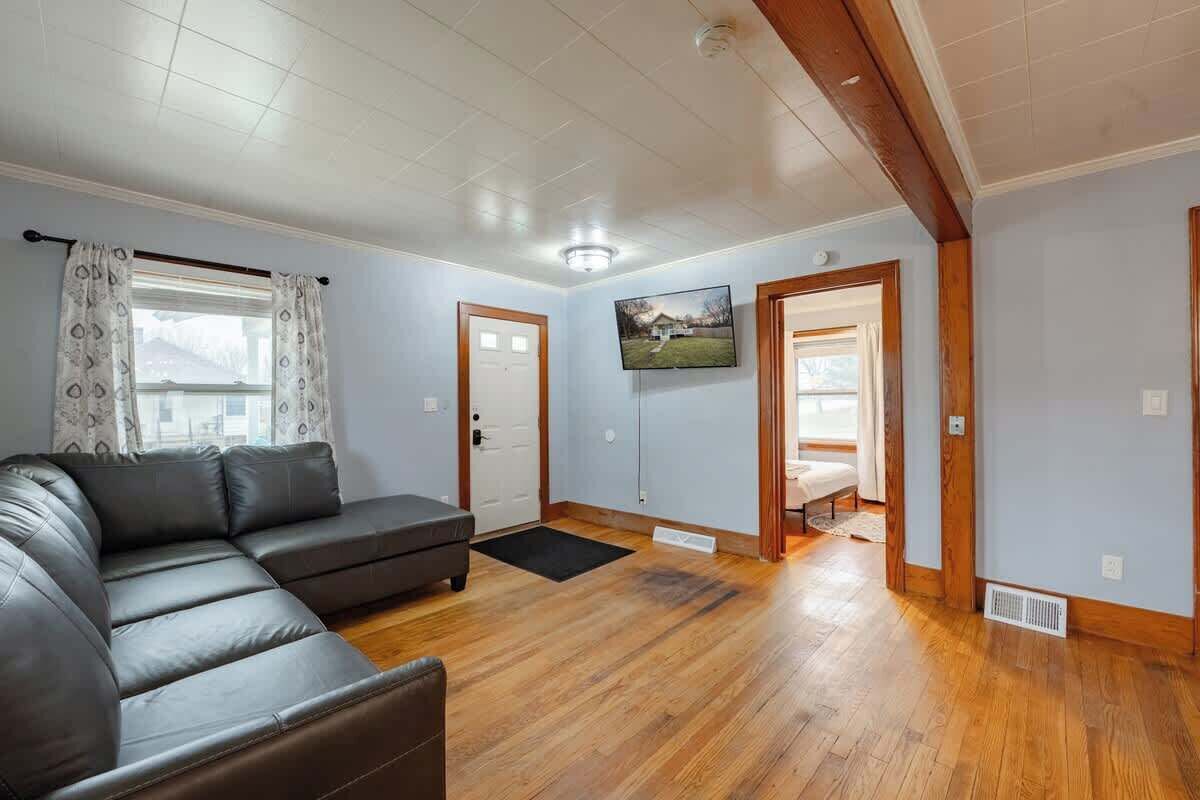 A living room with a sectional sofa, wooden flooring, a television mounted on the wall, and a door leading to another room.