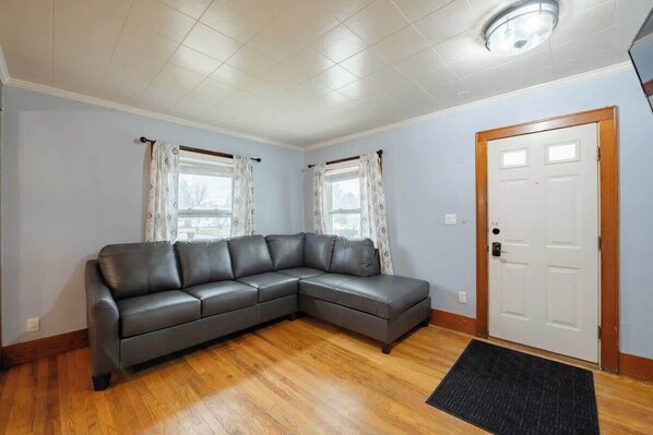 Un salon avec un canapé d’angle, une porte et une fenêtre avec des rideaux.