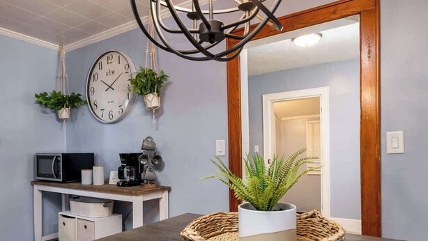 Une cuisine équipée d’une horloge, d’un four à micro-ondes, d’une machine à café et de plantes suspendues.