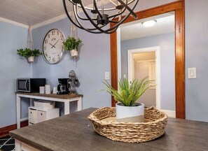 Une cuisine équipée d’une horloge, d’un four à micro-ondes, d’une machine à café et de plantes suspendues.