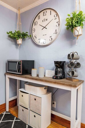 A kitchenette with a microwave, coffee maker, and a clock on the wall.