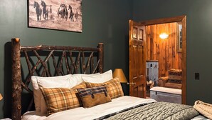A bedroom with a wooden headboard, a bed with multiple pillows, a bedside table, and a painting of horses on the wall. - Letchworth Farm Guesthouses (Nunda)