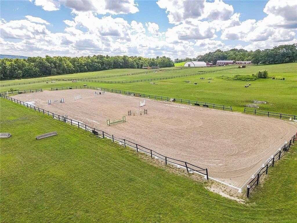 Una arena ecuestre con una pista de tierra, rodeada de campos verdes y una valla.