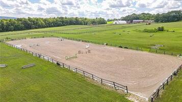 Una arena ecuestre con una pista de tierra, rodeada de campos verdes y una valla.
