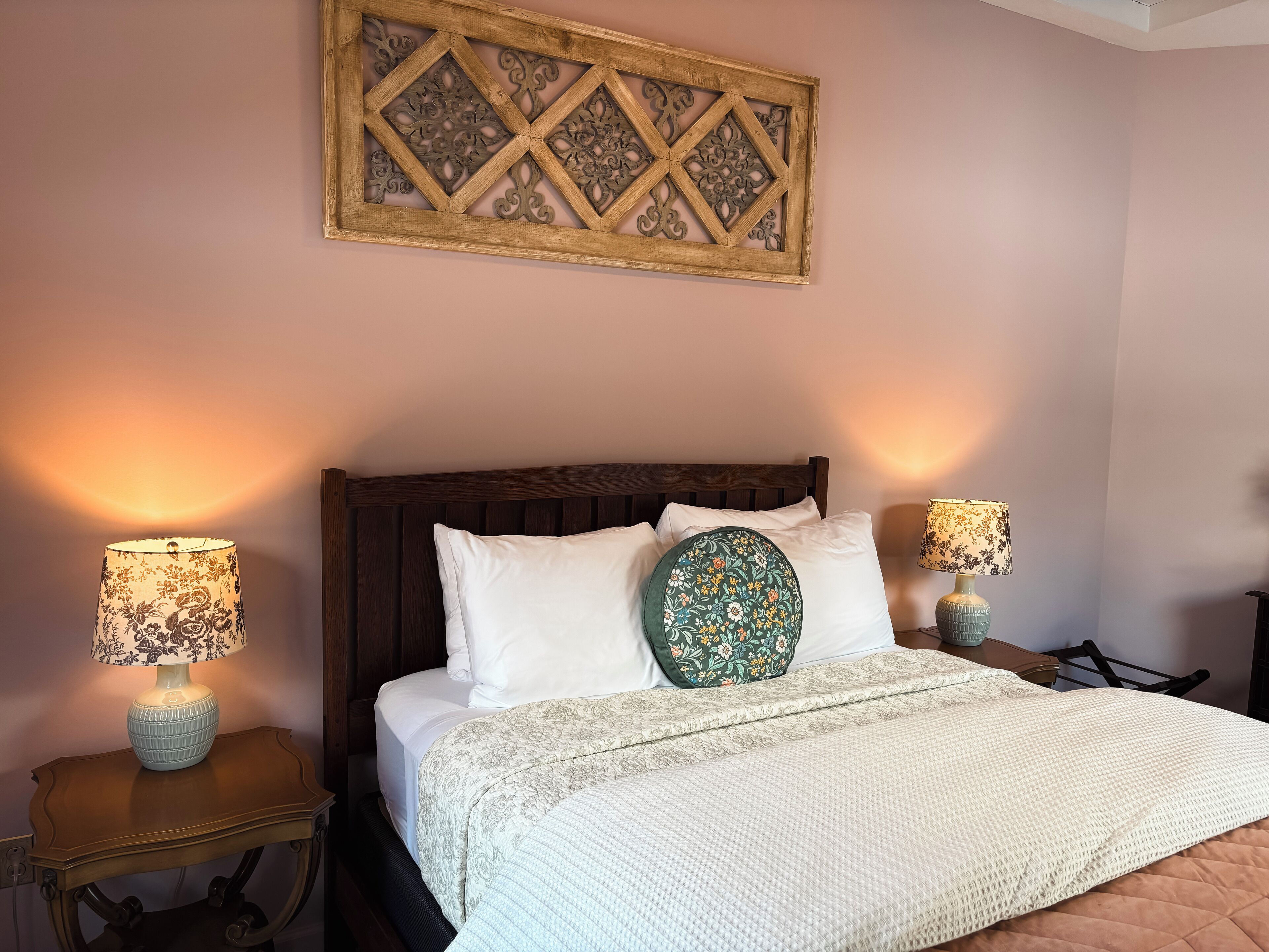 Una cama bien hecha con un edredón acolchado, dos lámparas de noche y un adorno decorativo sobre la cama.