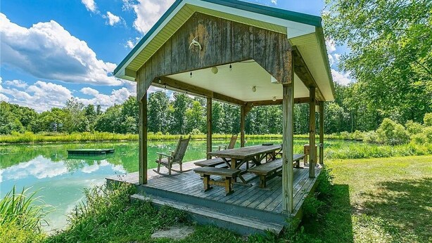 A wooden gazebo with a covered patio, surrounded by a pond and lush greenery. - Letchworth Farm Guesthouses (Nunda)