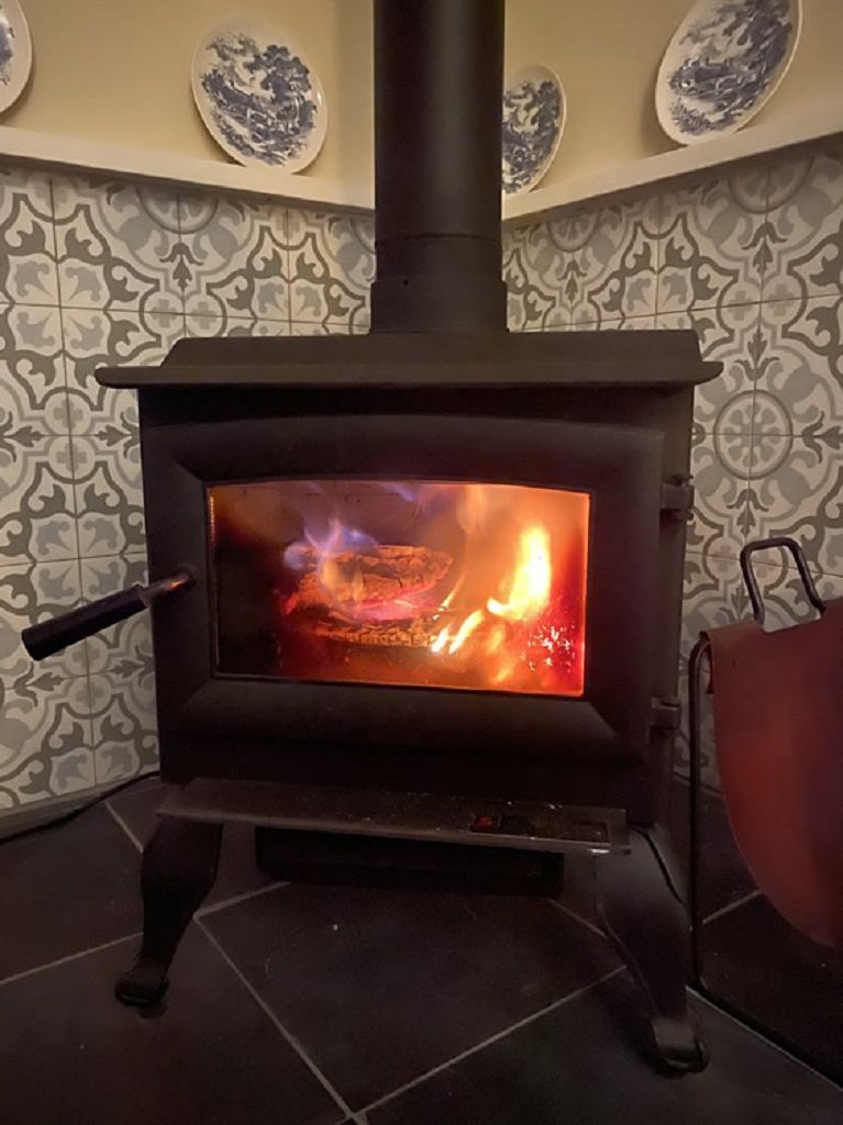 Un poêle à bois avec une façade en verre, placé devant un mur à motifs, au-dessus duquel sont disposées des assiettes décoratives.