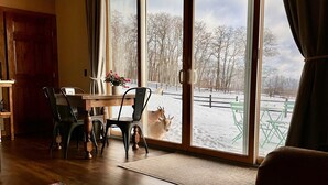 A cozy room with a dining area, large windows, and a view of a snowy landscape. - Letchworth Farm Guesthouses (Nunda)
