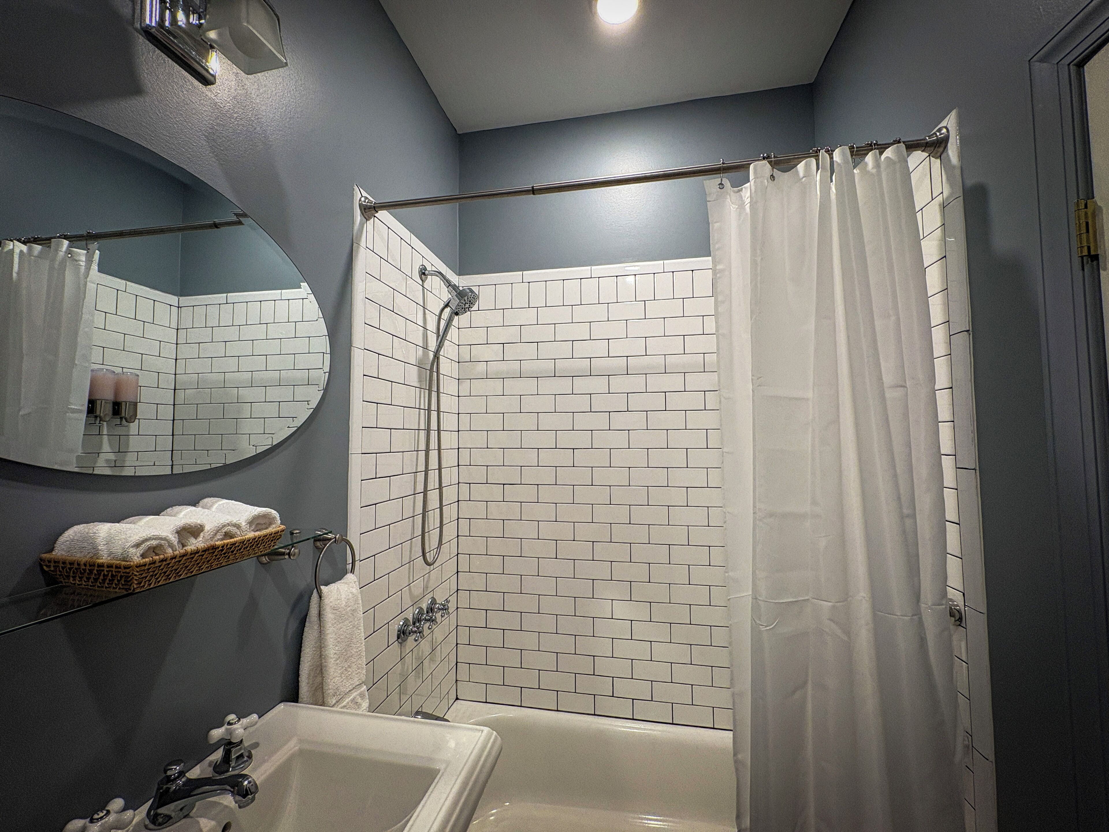 Un baño con una bañera blanca, una ducha con cortina blanca, un espejo y un estante con toallas.