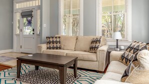 A living room with a beige sofa, a dark wooden coffee table, and patterned rugs. - Welcome to House on Hallett.  A historic home less than a mile from downtown (Mobile)