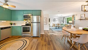 A modern kitchen with teal cabinets, stainless steel appliances, and a dining area with a wooden table and white chairs. - Cozy, Quiet and Peaceful Bailey's Harbor home: Close to Everything Door County! (Baileys Harbor)
