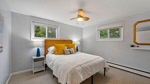 A bedroom with a bed, nightstand, lamp, ceiling fan, windows, and a wall-mounted mirror. - Cozy, Quiet and Peaceful Bailey's Harbor home: Close to Everything Door County! (Baileys Harbor)