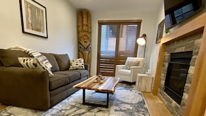 A living room with a sofa, a coffee table, a fireplace, and a patterned rug. - Spring Creek Luxury One Bedroom Sleeps 4 (Canmore)
