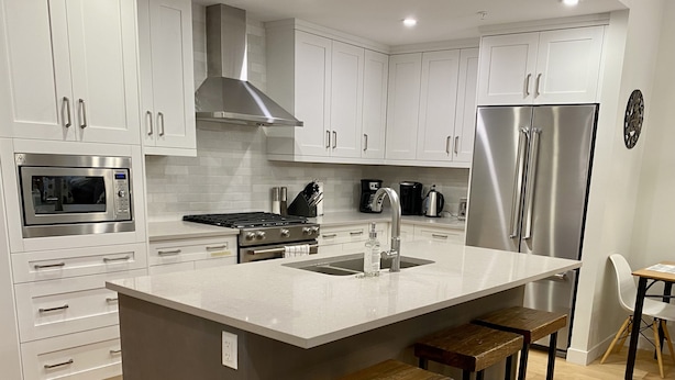A modern kitchen with white cabinetry, stainless steel appliances, a central island with bar stools, and a wooden floor. - Spring Creek Luxury One Bedroom Sleeps 4 (Canmore)