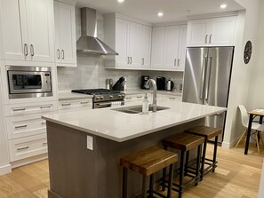 A modern kitchen with white cabinetry, stainless steel appliances, a central island with bar stools, and a wooden floor.