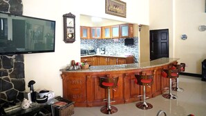 A kitchen with a bar area, wooden cabinets, a stone wall, a flat-screen TV, and a clock. - Quinta El Zable (Zaragoza)