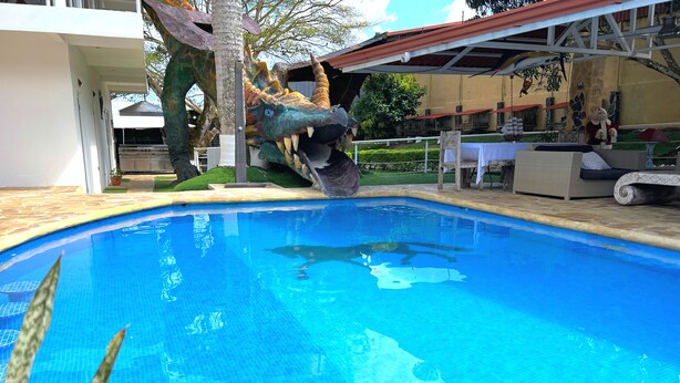 A swimming pool with a dinosaur statue, outdoor furniture, and a covered patio area. - Quinta El Zable (Zaragoza)