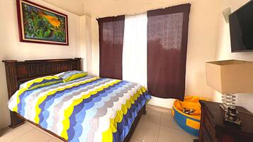 A bedroom with a bed, a painting, curtains, a television, and a dresser.