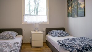 Une chambre avec deux lits, une table de chevet, une lampe et une fenêtre donnant sur des arbres.