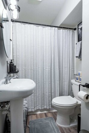 A bathroom with a white sink, toilet, and shower curtain. - Remote Ready I 2 BR 1 BA (Lansing)