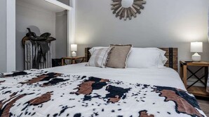 Een slaapkamer met een bed, twee nachtkastjes, een spiegel aan de muur en een deur naar een andere kamer.