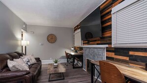Een moderne woonkamer met een bruine leren bank, een houten salontafel, een eethoek met een tafel en stoelen, en een open haard met een metselwerk accentmuur.