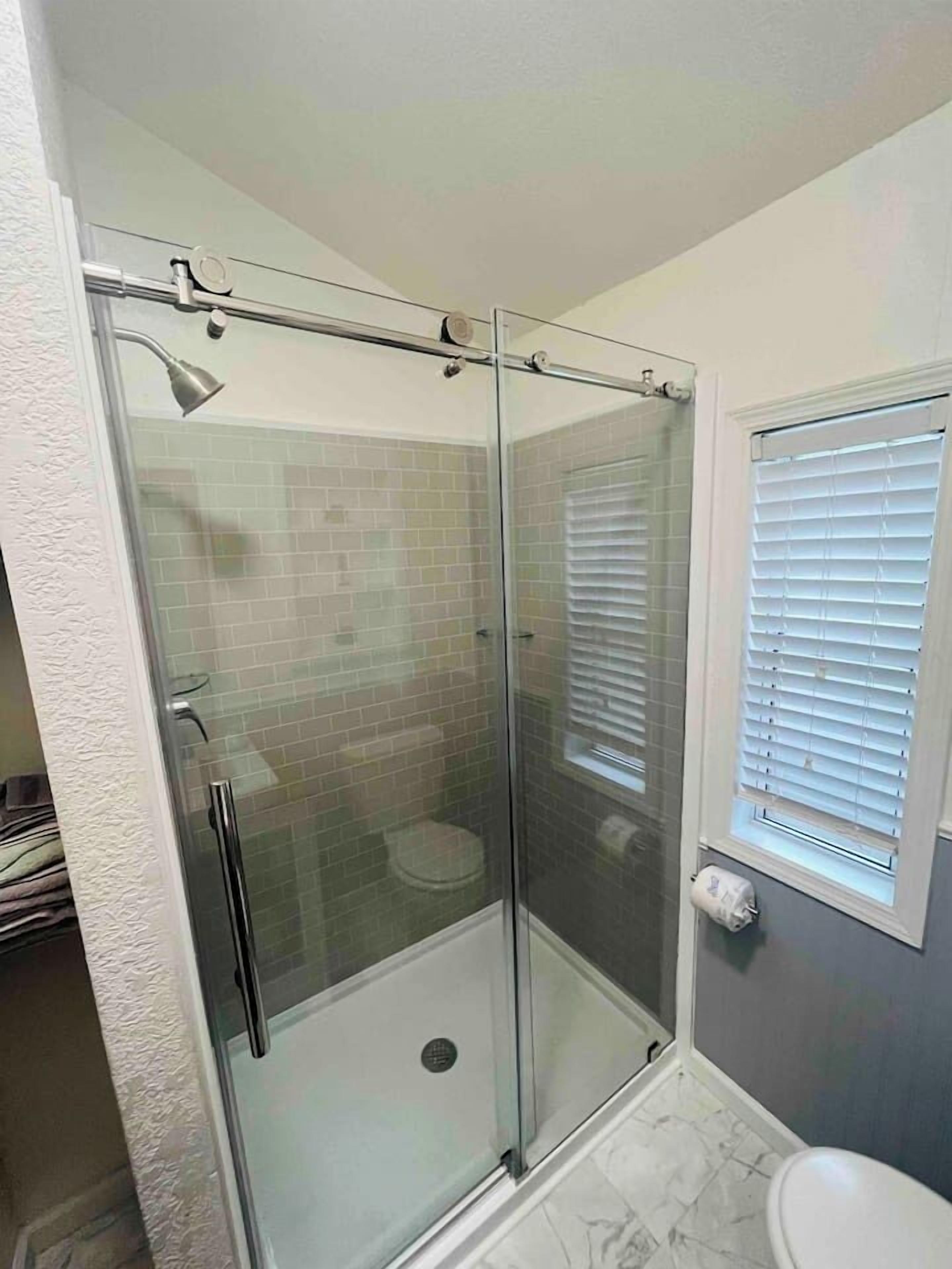 Lasiseinöillä varustettu suihkutila, jossa on käsisuihku, wc ja ikkuna, jossa on sälekaihtimet.