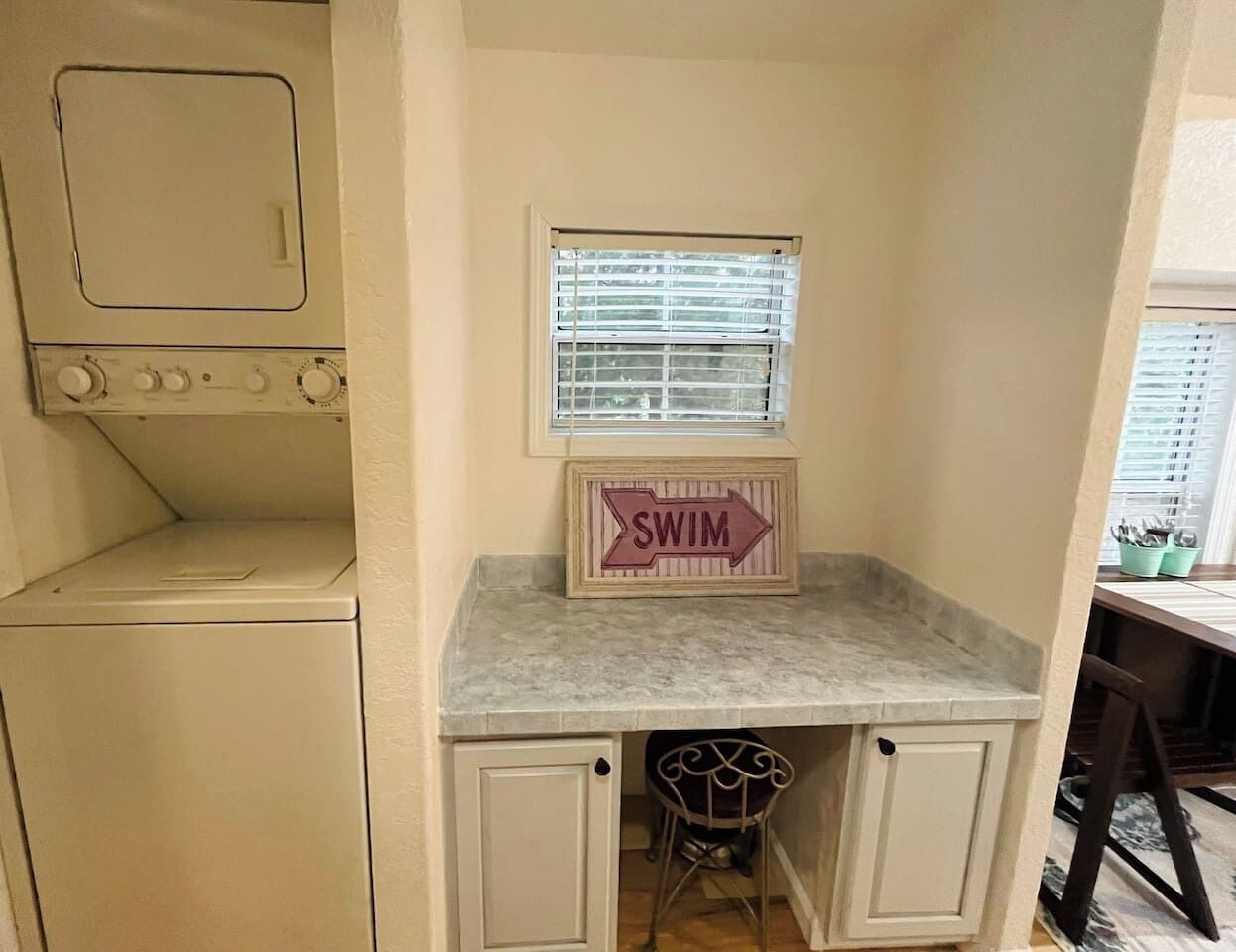 A compact kitchen with a built-in washer and dryer, a small window with blinds, and a 'SWIM' sign on the countertop.
